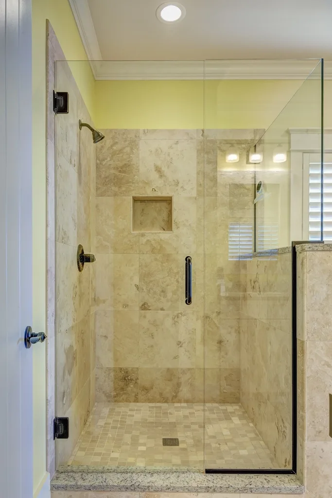 Travertine shower behind frameless glass